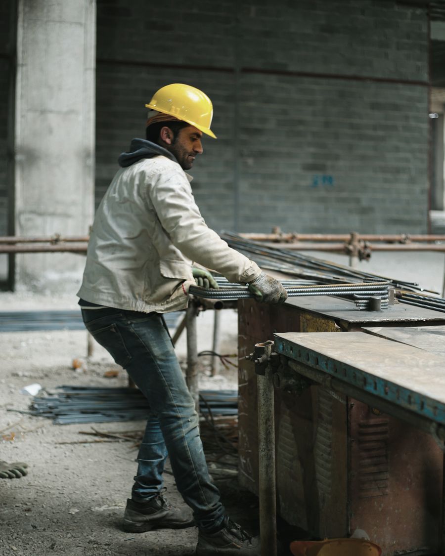 A worker in a yellow hard hat and work gloves cutting steel rebar on a construction site