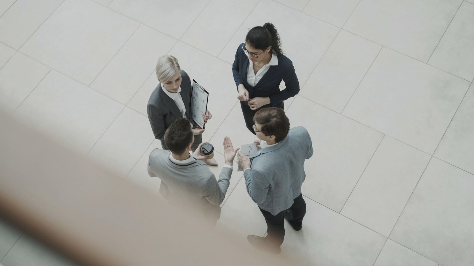Four colleagues in business suits talking in an office lobby, seen from the floor above